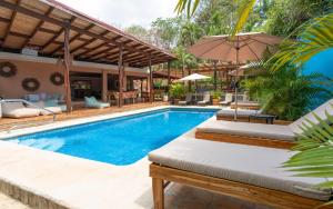 uma piscina com cadeiras e um guarda-sol ao lado de uma casa em Hotel Arco Iris em Tamarindo