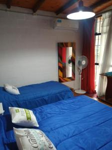 two beds in a room with blue sheets and a fan at ALOJAMIENTO SERRANO in Villa Giardino