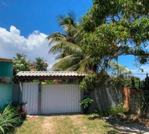 a white fence in front of a house with a palm tree at Casa Alto Padrão - Condomínio Paradise Ponta da Areia in São Pedro da Aldeia +2 photos