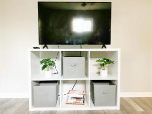 a tv on a white entertainment center with two plants at SFA Retreat, Spacious Downtown Apartment in Nacogdoches