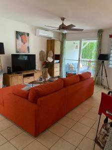 an orange couch in a living room with a flat screen tv at Residence piscine Ste Roses in Îlet à Christophe