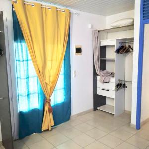a bedroom with a yellow curtain and a closet at La petite Golondrina - Appartement T2 chaleureux dans un cadre paisible verdoyant in Ducos
