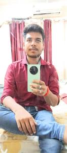 Un hombre sentado en el suelo sosteniendo un teléfono celular. en Kishan guest house, en Ayodhya