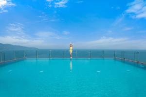 岘港Canvas Danang Beach Hotel的一名女子站在海边的游泳池边