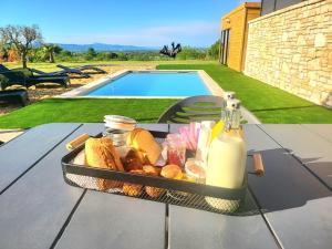 un plateau de pain et de lait sur une table à côté d'une piscine dans l'établissement Gîte de charme L'Escale Des Sens sauna et jacuzzi privé sud Ardéche, à Bessas