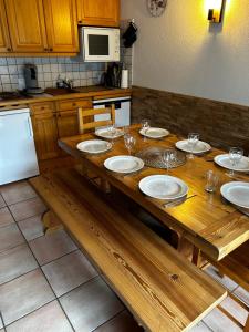 a wooden table with plates and wine glasses on it at Charmant appartement 6-8 personnes au cœur du village à proximité lac et pistes de ski in Morillon