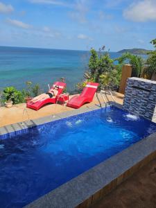 a swimming pool with two lawn chairs and the ocean at Masamirey Hilltop Cottage with Mini Pool and Beach Access & WIFI in Sual
