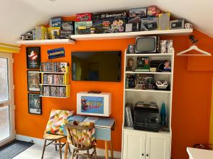 a room with an orange wall with a tv and shelves at Cherry Cottage Retro Stay, Stourport-on-Severn in Stourport