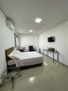 a white bedroom with a bed and a tv at Suíte com entrada individual in Sinop