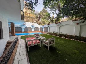 a yard with two benches and a table and a pool at Villa Maadi 35 -R 101- Terrace View Room in Cairo