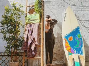 a woman standing next to a surfboard on a rack at Coastal Garden Paradise Retreat- 6 min from the beach in Charneca