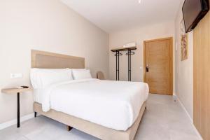 a bedroom with a large white bed and a television at Hostal Puerta Almar in Estepona