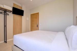 a bedroom with a white bed and a television at Hostal Puerta Almar in Estepona