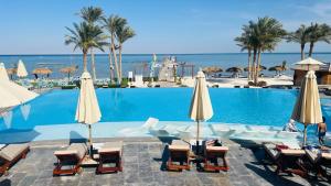 a swimming pool with chairs and umbrellas and the ocean at Villa Private pool cancun El Ain El Sokhna 63 in Ain Sokhna