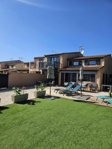 un bâtiment avec une cour avec des chaises et une pelouse dans l'établissement Maison tout confort 4 ch 8p domaine privé avec piscines, et plage à 10 min à pied, à Portiragnes