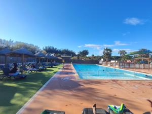 a swimming pool at a resort with people sitting on chairs at Mobil-home climatisé Plage à 3 min Proche Barcarès Piscine chauffée in Torreilles
