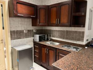 une cuisine avec des armoires en bois, un évier et un micro-ondes dans l'établissement Modern Studio 1BR, Celia TMG, New Administrative, New Capital, Fully Equipped, King Bed, Ground Floor, à Kafr ash Sharā‘inah 1 autre photo