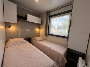 zwei Betten in einem kleinen Zimmer mit Fenster in der Unterkunft Un toit sur le bassin Bungalow solaire in Lège-Cap-Ferret