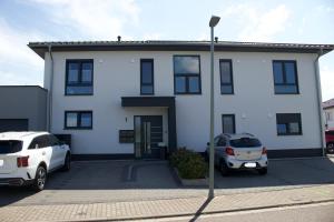 a white house with two cars parked in a parking lot at Ferienwohnung Dariana Schwalbach/Saar in Schwalbach