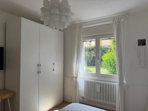 a white bedroom with a window and a chandelier at L'angolino apartment in Trento