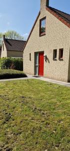 a brick house with a red door and a yard at Lakefront Cottage Gelderland BBQ & tuin 6pers in Ewijk