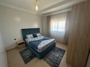 a bedroom with a bed with a blue headboard and a window at Appartement à Houma, proche Port Tanger Med in Dalia