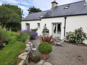 a white house with a chair and a garden at Drummin Cottage in Tinahely