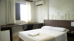 a bedroom with a bed with a desk and a window at Abbas Hotel in Uberlândia