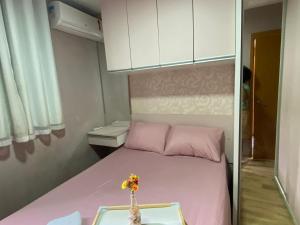 a small bedroom with a pink bed with a vase with flowers at Doce lar da Be in Ribeirão Preto