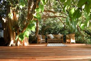 a wooden deck with chairs and a couch under a tree at De Nest - Clear Glass Tree Cabin in Montagu
