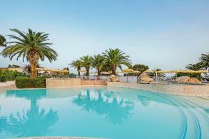 a large swimming pool with palm trees and umbrellas at Aldiana Club Rocca Nettuno Calabria in Tropea