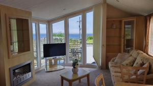 Seaside chalet in Ardmore with breathtaking views في أردمور: غرفة معيشة بها أريكة وتلفزيون وبعض النوافذ