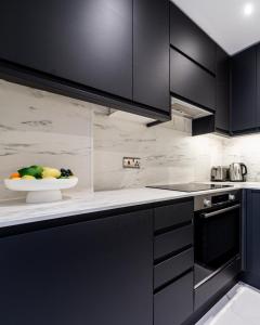 a kitchen with black cabinets and a bowl of fruit at Kensington Prime Apartments in London