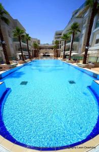 een groot blauw zwembad met palmbomen en gebouwen bij Garden Beach Luxury Apartment in Eilat