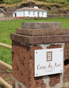 a sign on a brick wall with a house in the background at Casa da Avó - Turismo Rural in Santo Espírito