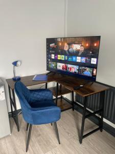 a desk with a television and a blue chair at 1 Bed Flat with King or Twin Beds, Sofa Bed, Work space, Dining and SMART TV with Free Wifi Throughout! in Wingate