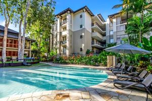 a swimming pool with chairs and an umbrella in front of a building at Vista Verde - A Temple Resort Family Treasure in Palm Cove