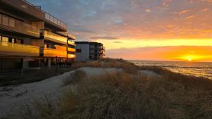 a sunset on the beach with a building and the ocean at Gardenia Sea Side MARTINA 1 Dziwnów in Dziwnów