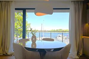 a dining room with a table and chairs and a large window at Marina Ostróda IV - super widok na jezioro, 10 m do wody, taras i balkon, winda, klima, garaż in Ostróda +14 photos