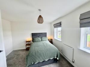 a bedroom with a bed with a green comforter and two windows at Upper Townhouse, Exeter in Alphington