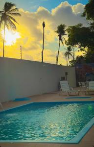 a swimming pool with palm trees and a sunset at Chácara Amsterdam in Aracaju
