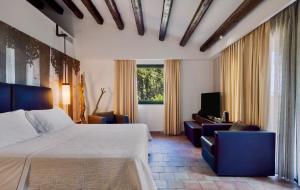 a hotel room with a bed and chairs and a television at Vallegrande Nature Resort by Geocharme in Cefalù +37 photos