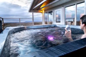 ein Mann in einer Whirlpool-Badewanne mit einem Mobiltelefon in der Unterkunft Cabin in Faukás, west part of Iceland - Birta Rentals in Fossatún