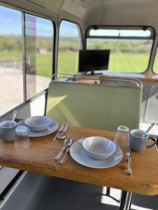 a wooden table with plates and cups and utensils on it at Cornwalls Vintage Camping Bus in Delabole