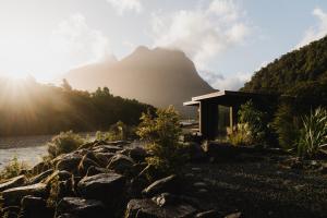 a house next to a river with a mountain in the background at Milford Sound Lodge in Milford Sound