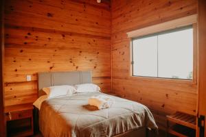 a bedroom with wooden walls and a bed with a window at Chalés Bosque das Oliveiras in Urubici