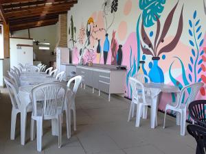 a dining room with white tables and chairs and a mural at PORTO SUÍTES PERUÍBE CHECK-OUT LIVRE aos DOMINGOS in Peruíbe