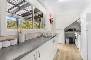 eine Küche mit weißen Schränken und einer Spüle und einem Fenster in der Unterkunft Madigan Cottages - Australiana in Lovedale