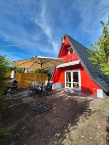 a red house with a table and chairs and an umbrella at Ferienhaus am Helenesee 5 in Frankfurt Oder