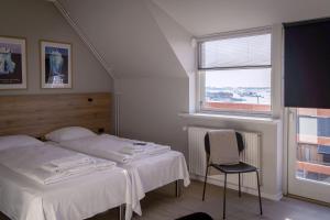 a bedroom with two beds and a chair and a window at HOTEL SØMA Ilulissat in Ilulissat